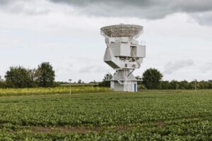 A large satellite antenna stands prominently in a lush field in Riedstadt, Germany.